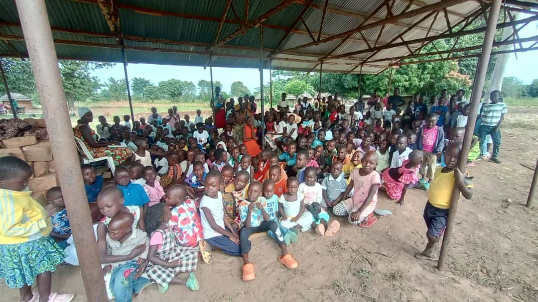 Children seated together under a covered community shelter.