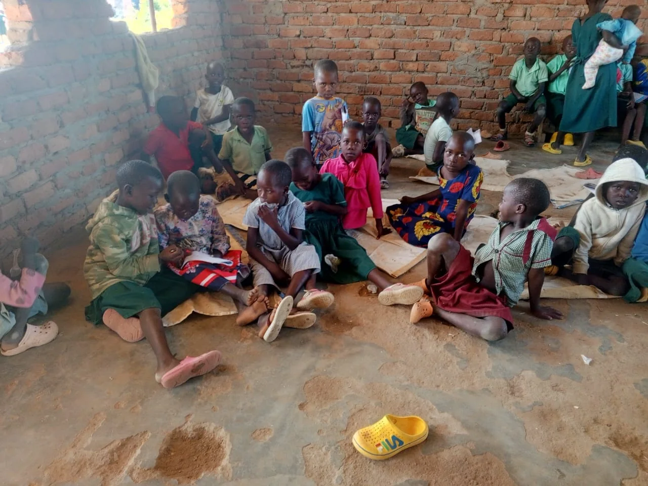 Children seated together for a learning activity inside a simple brick room