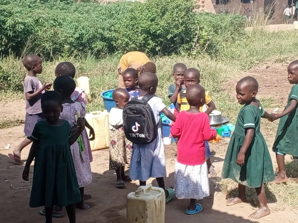 Children gathered near water containers during an outdoor community activity.
