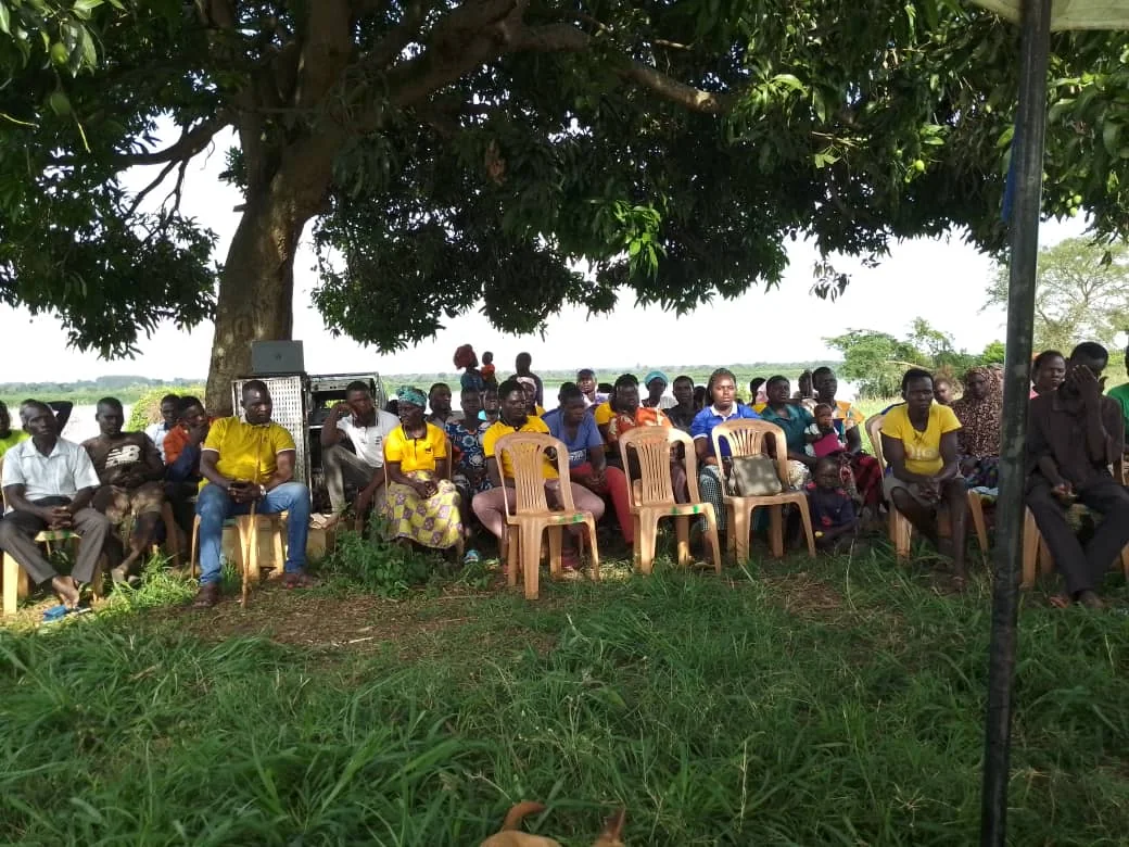 Families and community members gathered outdoors beneath a large tree