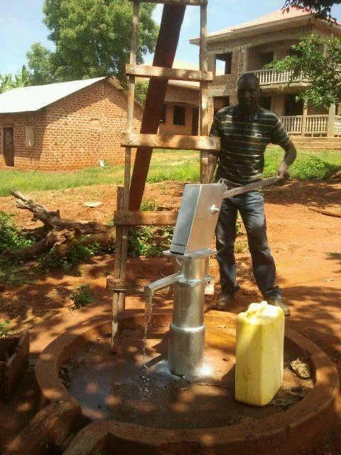 A community member operating a metal hand pump beside a yellow water container