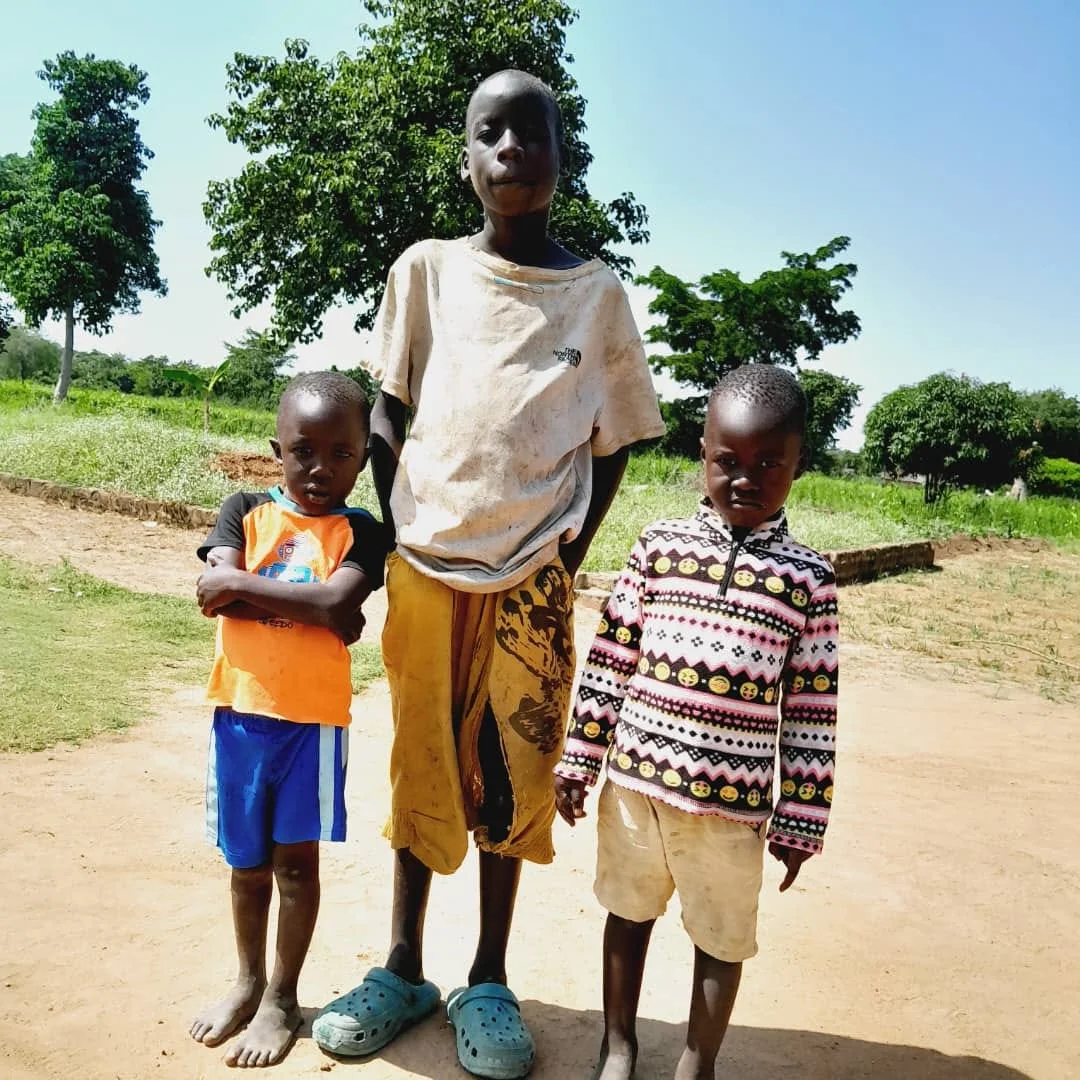 Three children standing together outdoors in their community.