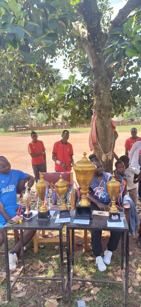 Youth and volunteers seated near sports trophies during an outdoor activity.